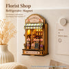 A wooden florist shop refrigerator magnet display featuring flowers and a sign.