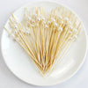 A heart shape arrangement of pearl-tipped bamboo cocktail picks on a white plate.