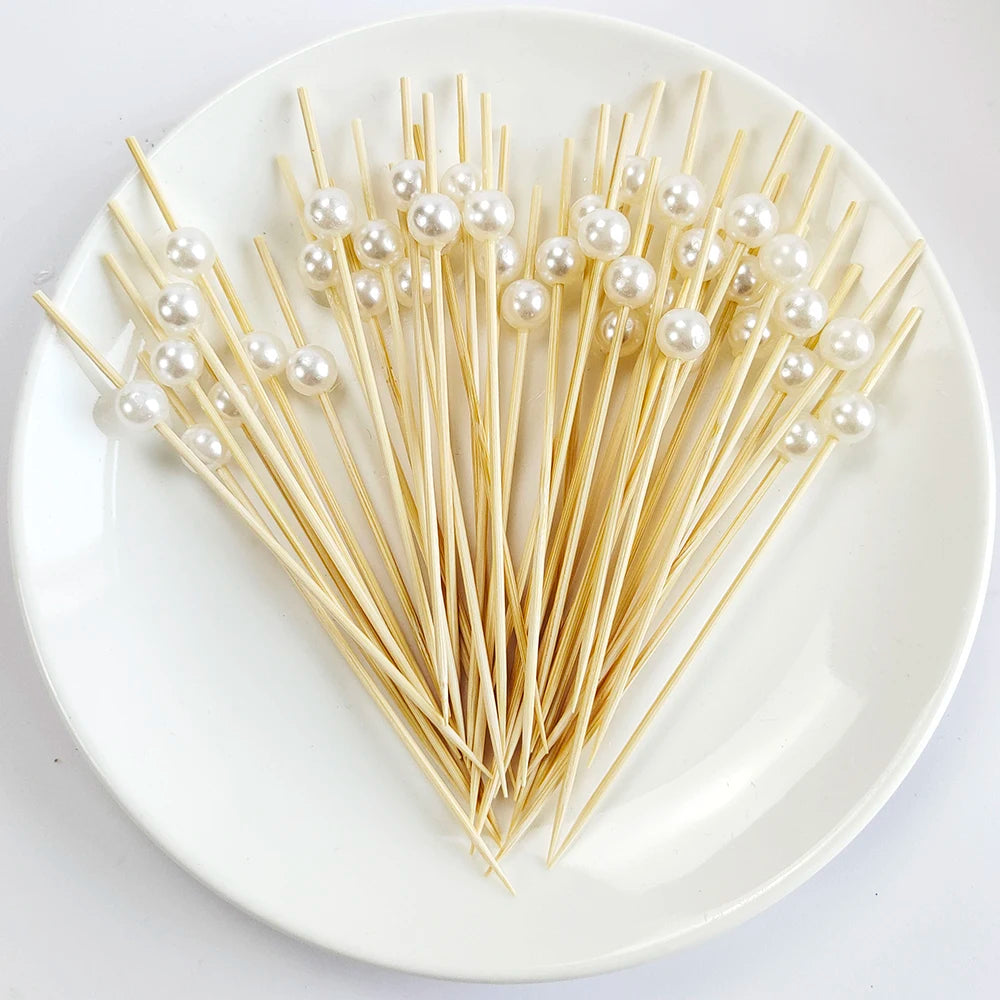 A heart shape arrangement of pearl-tipped bamboo cocktail picks on a white plate.