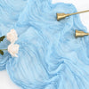 Light blue cheesecloth table runner with gold metal accents and white roses on a white background