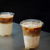 A tall plastic cup filled with iced coffee or a layered beverage is shown against a dark background.