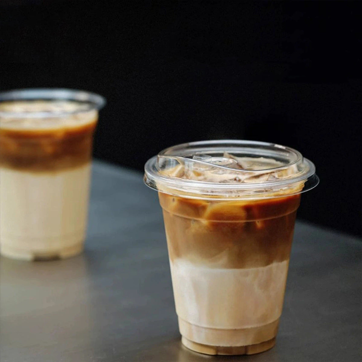 A tall plastic cup filled with iced coffee or a layered beverage is shown against a dark background.
