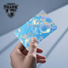 A hand holds a holographic cat credit card skin sticker with iridescent blue and gold accents.