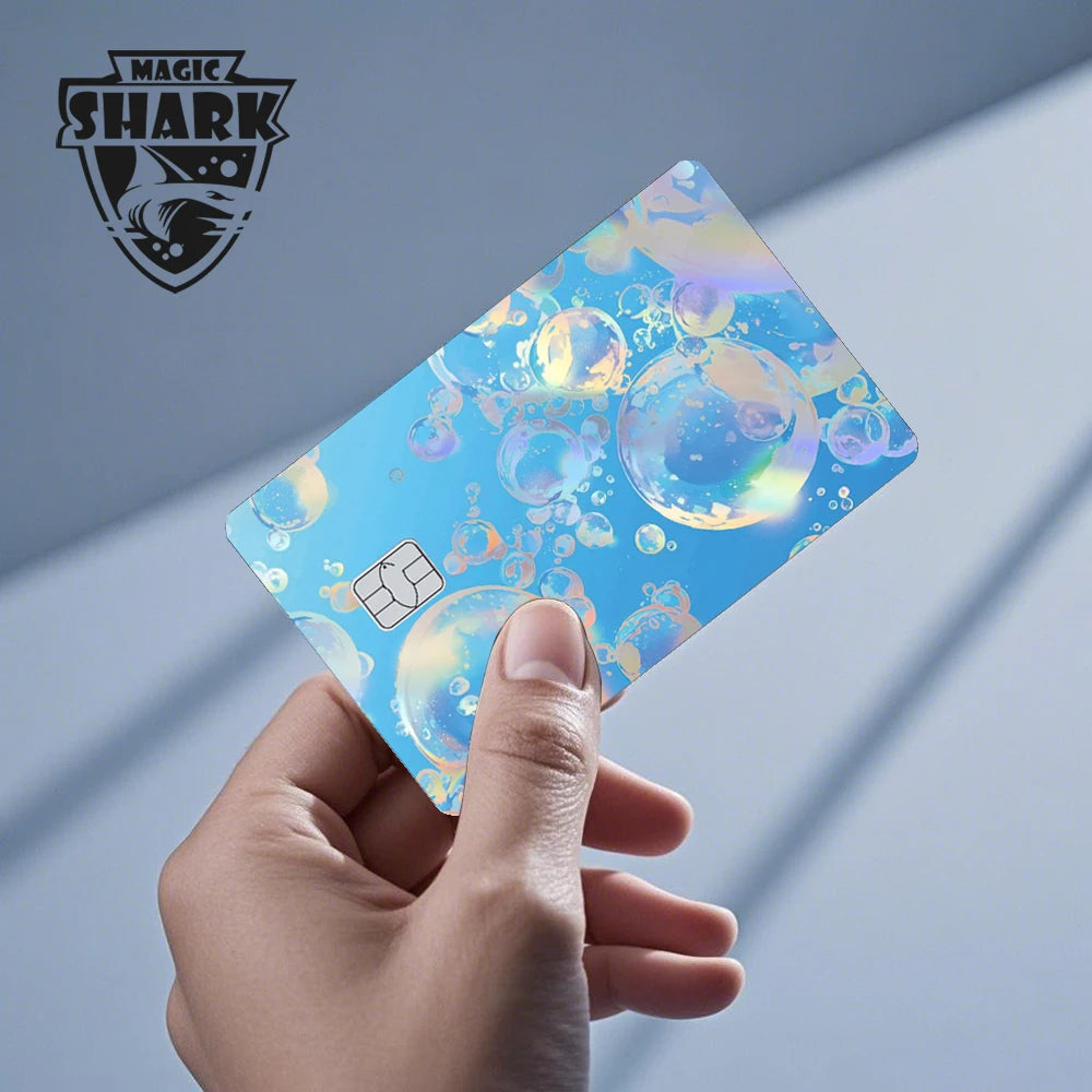 A hand holds a holographic cat credit card skin sticker with iridescent blue and gold accents.