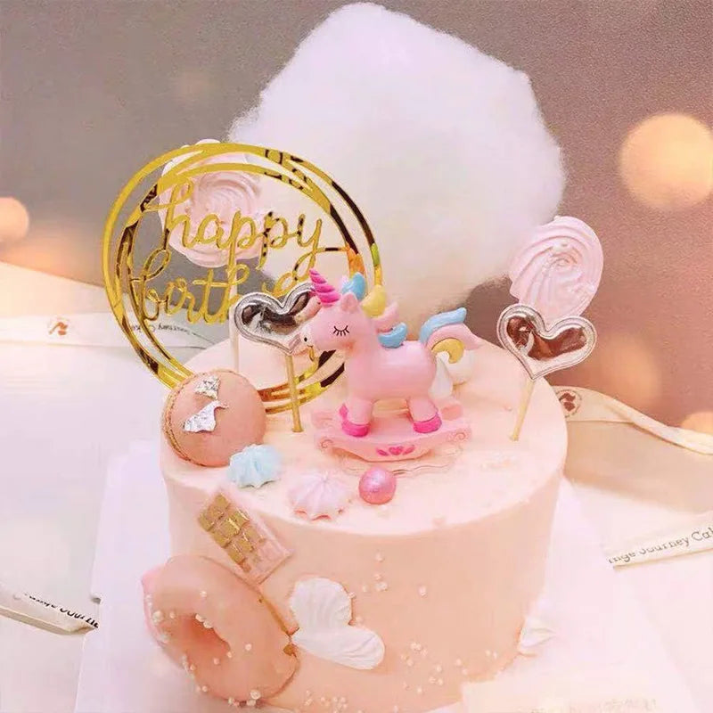 A pink cake decorated with edible flowers and a unicorn figurine, surrounded by a large white cloud and gold accents.