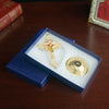 A gold metal Jesus cross ornament with a decorative base is displayed in a blue velvet box on a wooden surface.
