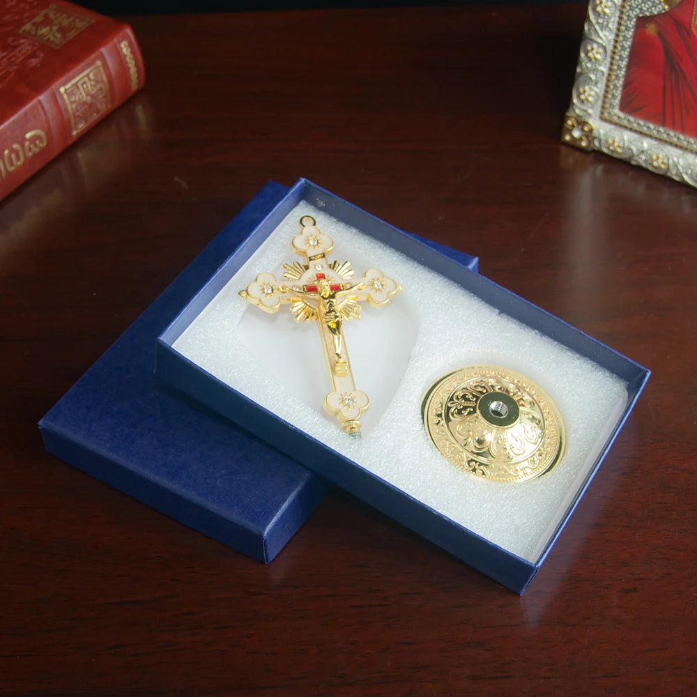 A gold metal Jesus cross ornament with a decorative base is displayed in a blue velvet box on a wooden surface.