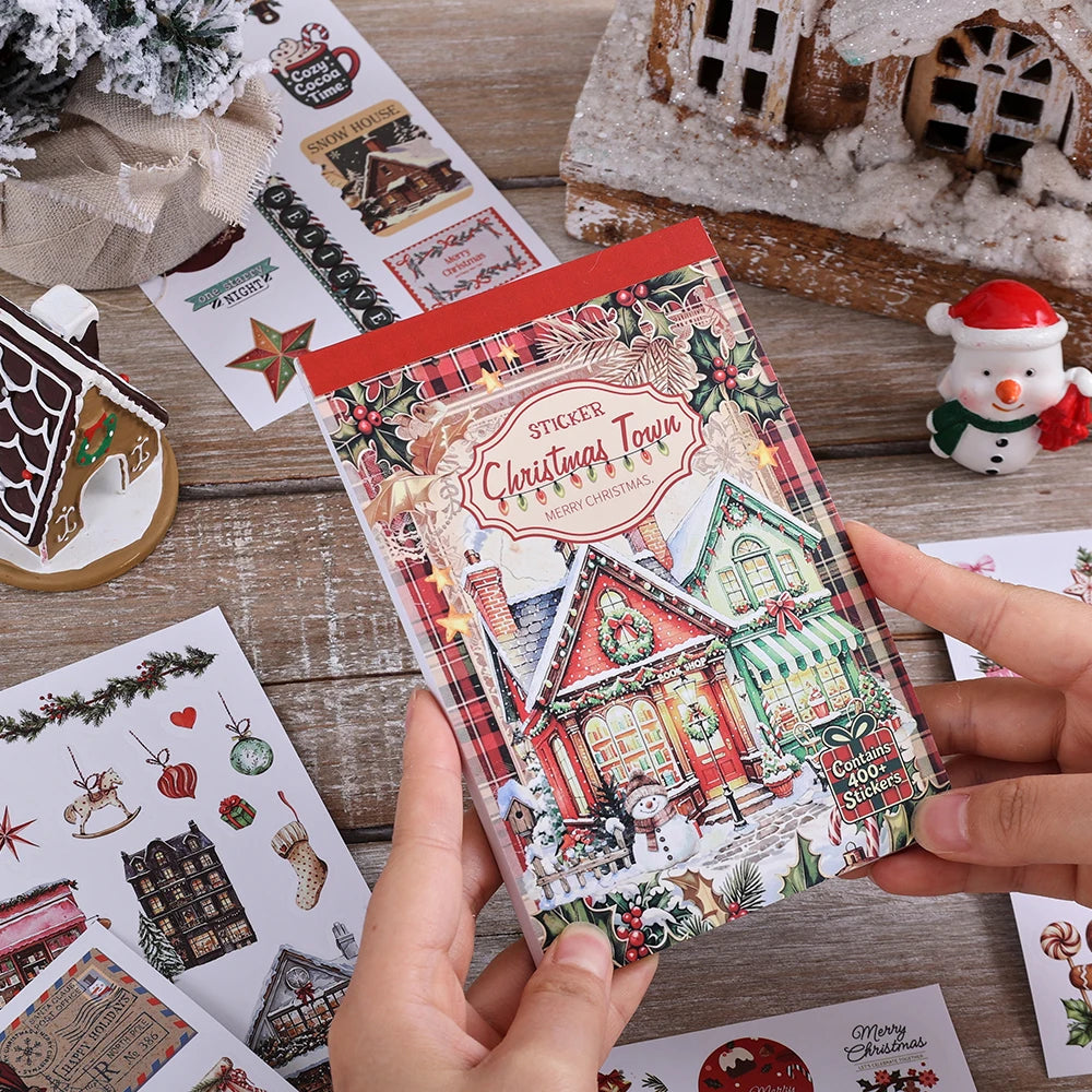 Eine Hand hält ein Blatt festlicher Weihnachtsstickers mit Weihnachtsdorf- und Winterelementen.