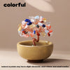Handcrafted crystal tree with colorful stones mounted on a copper wire base in a light stone bowl.