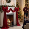 A fireplace decorated with a red velvet bow and streamers, set against a backdrop of a lit Christmas tree.