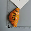 A golden bread-shaped object with the word BREAD written on it, photographed next to a ruler.