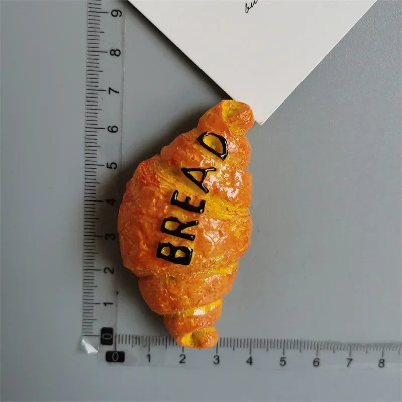 A golden bread-shaped object with the word BREAD written on it, photographed next to a ruler.