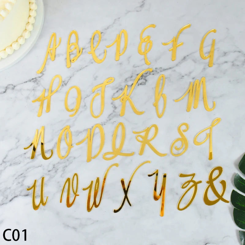 A set of gold acrylic alphabet and numeral cake toppers displayed on a white marble surface.
