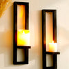 A rustic wooden wall shelf holds a glowing yellow candle, mounted on a white wall.