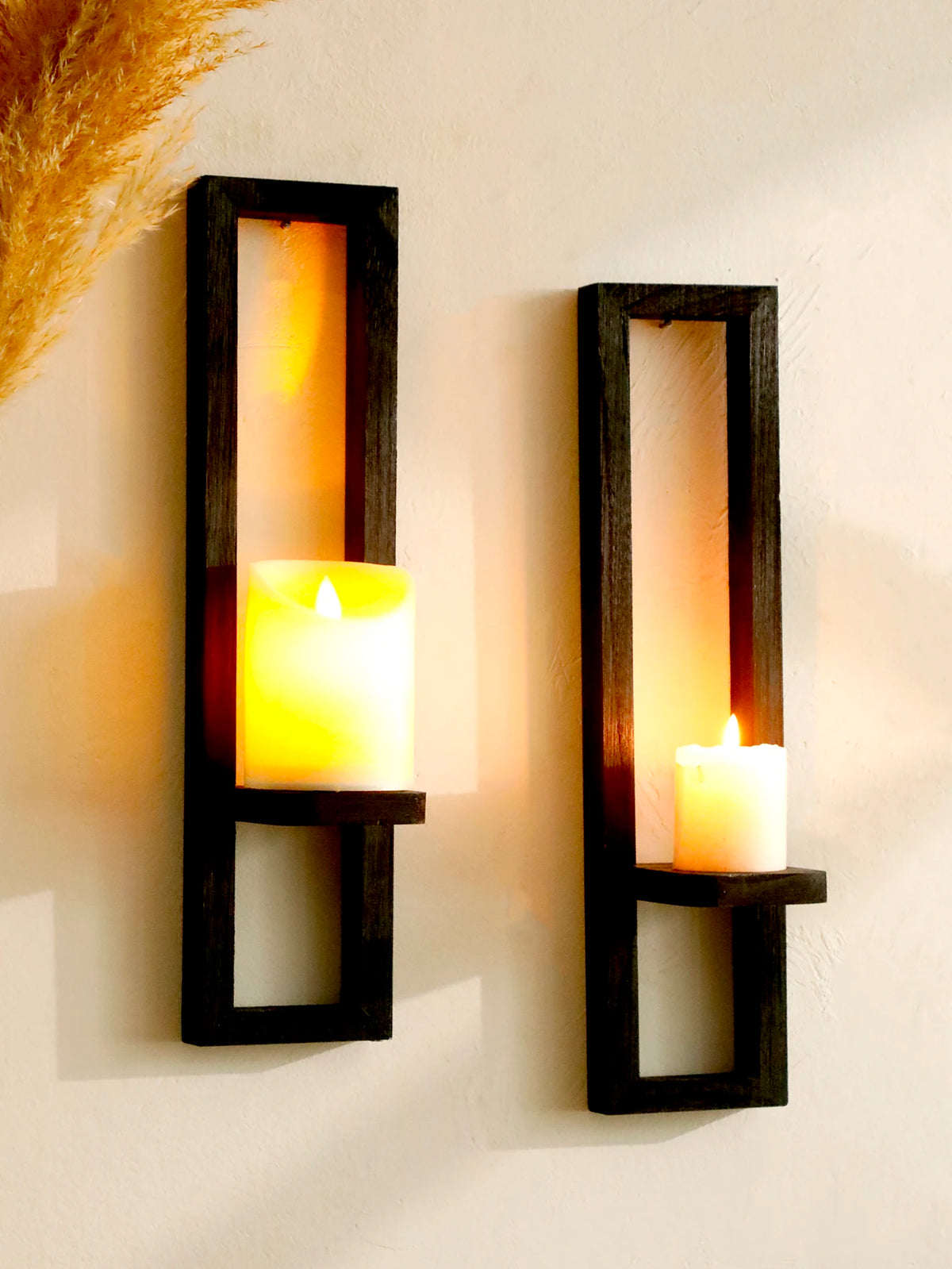 A rustic wooden wall shelf holds a glowing yellow candle, mounted on a white wall.