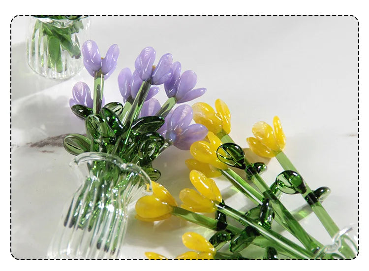 A bouquet of handmade glass flowers in shades of purple and yellow displayed in a clear glass vase.