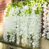 Cascade de fleurs artificielles de wisteria blanches drapées sur un mur de briques.