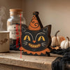 A wooden cat face Halloween decor set with orange and black paint, resting on a rustic wooden surface.