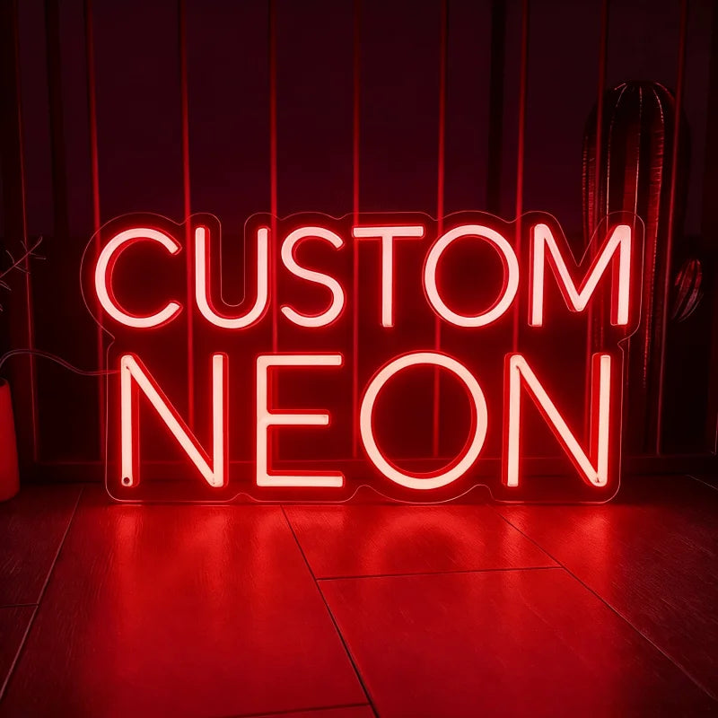 A bright red neon sign spelling out CUSTOM NEON is displayed on a dark wooden floor.