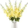 Un bouquet de fleurs artificielles de delphiniums jaunes et blancs dans un vase blanc.