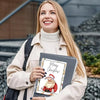 A blonde woman wearing a beige coat holds a spiral-bound Christmas gift card book featuring a Santa Claus illustration.