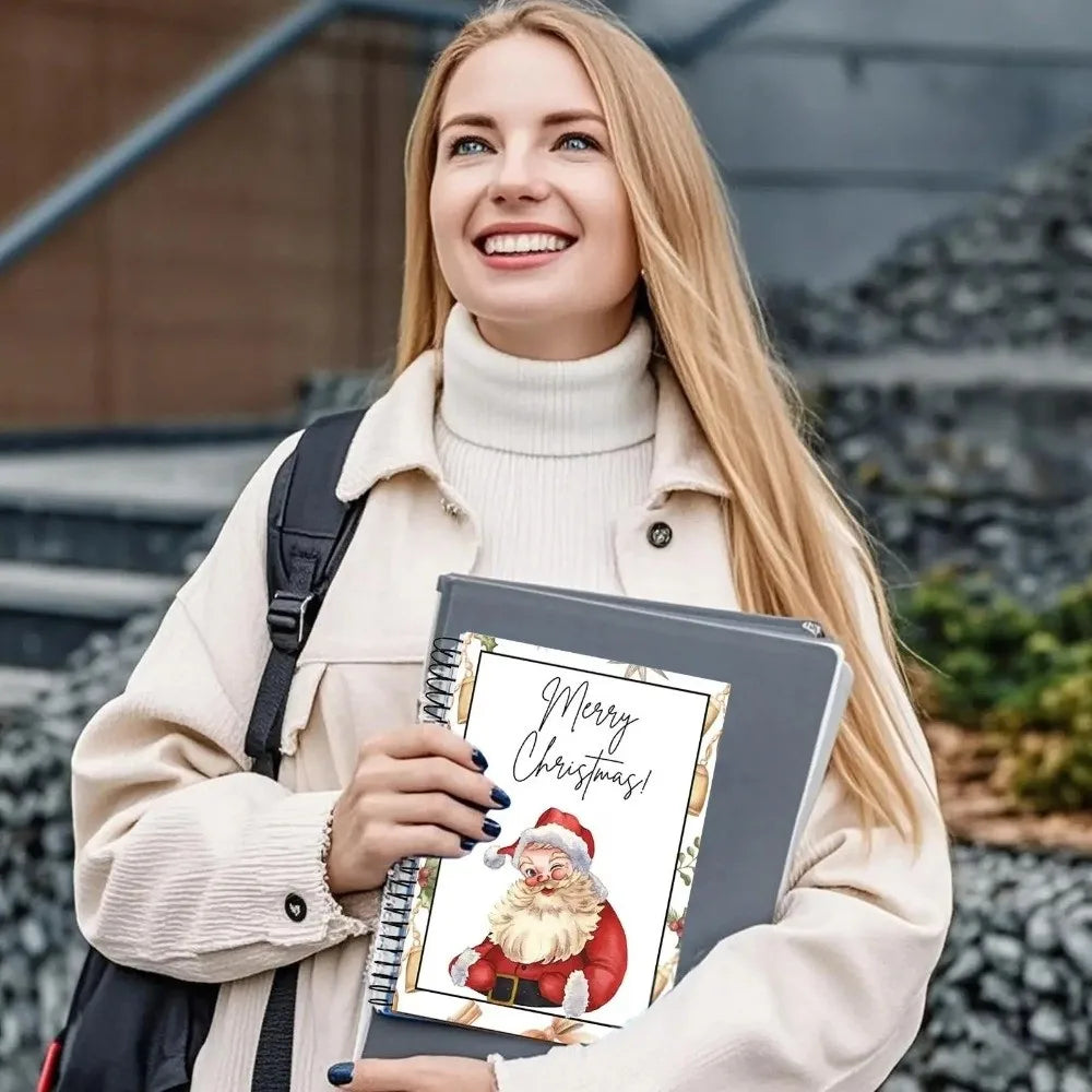 A blonde woman wearing a beige coat holds a spiral-bound Christmas gift card book featuring a Santa Claus illustration.