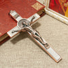 A silver crucifix featuring a sculpted figure of Christ, St. Benedict medal, and INRI inscription, displayed on a wooden book