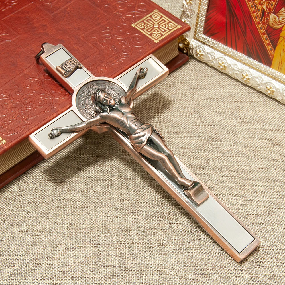 A silver crucifix featuring a sculpted figure of Christ, St. Benedict medal, and INRI inscription, displayed on a wooden book