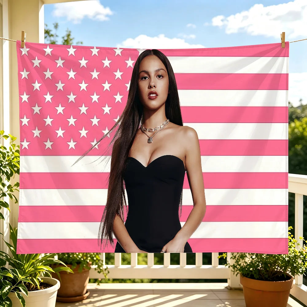 A woman wearing a black strapless dress stands in front of a pink and white striped flag tapestry.