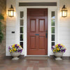 A brown wooden front door surrounded by white trim and flanked by decorative lanterns, with potted purple and yellow pansy fl