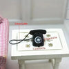 A black retro rotary desk phone miniature with a cord is displayed on a white surface.