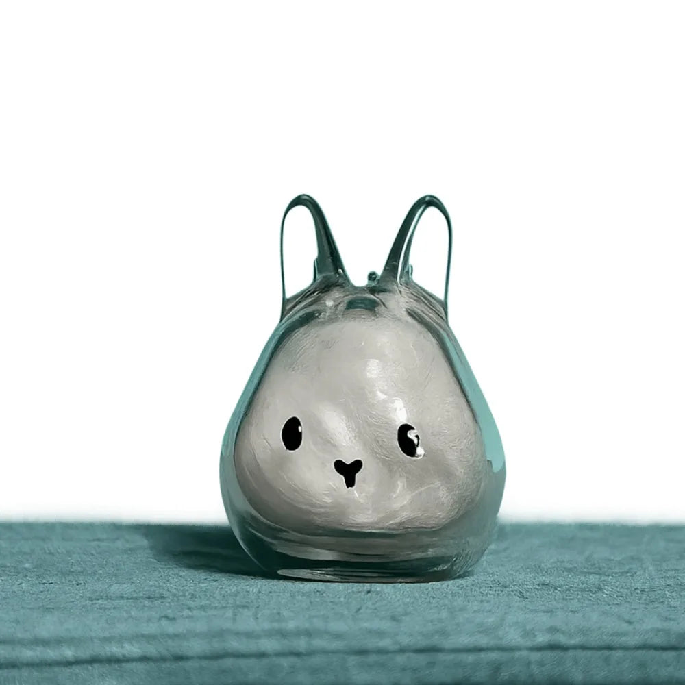 A clear glass figurine shaped like a rabbit with long ears, resting on a teal surface.