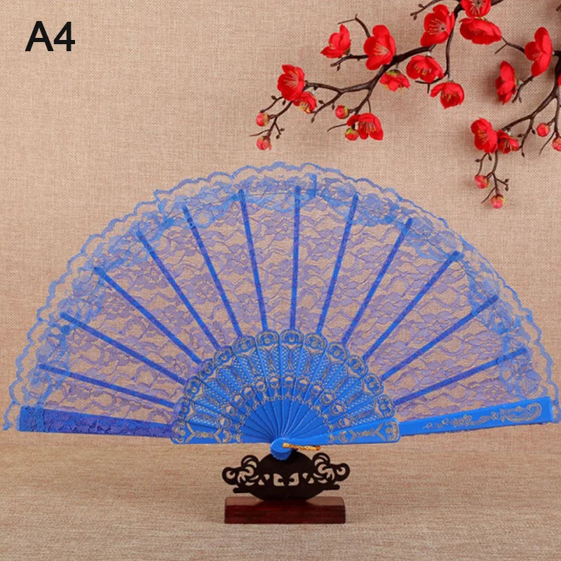 A blue lace folding hand fan with a black base is displayed against a background of red blossoms.