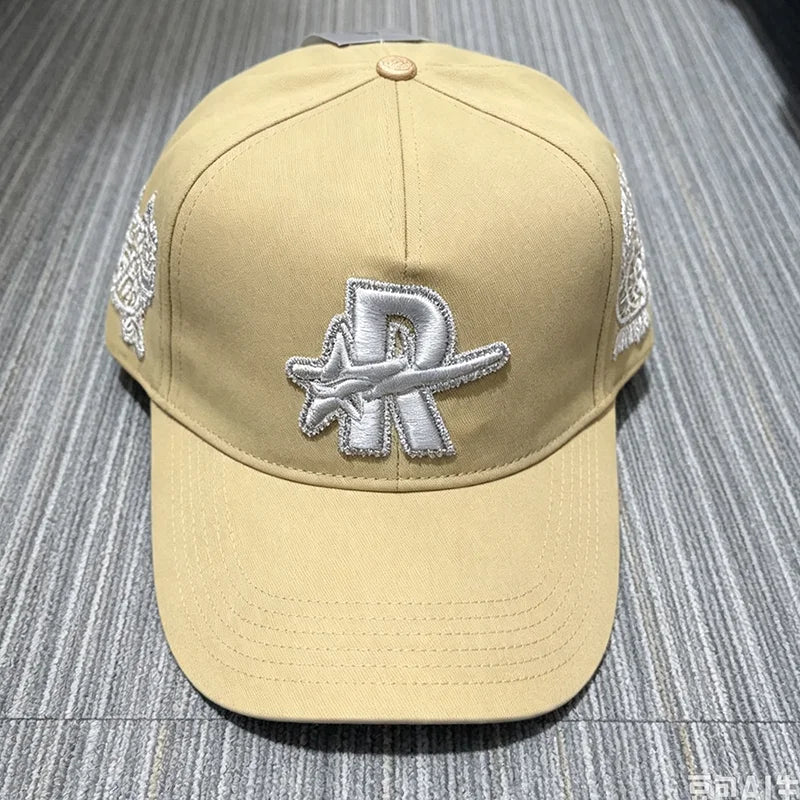 A beige baseball cap embroidered with a silver star design and white stitching on the sides.