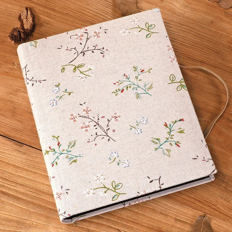 A beige linen photo album with a delicate floral pattern lies on a wooden surface.