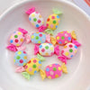 A collection of 20 colorful resin candy charms in various shapes and colors arranged on a white plate.