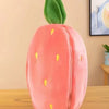 A pink plush strawberry with green leaves and a bunny-shaped pillow on a wooden surface.