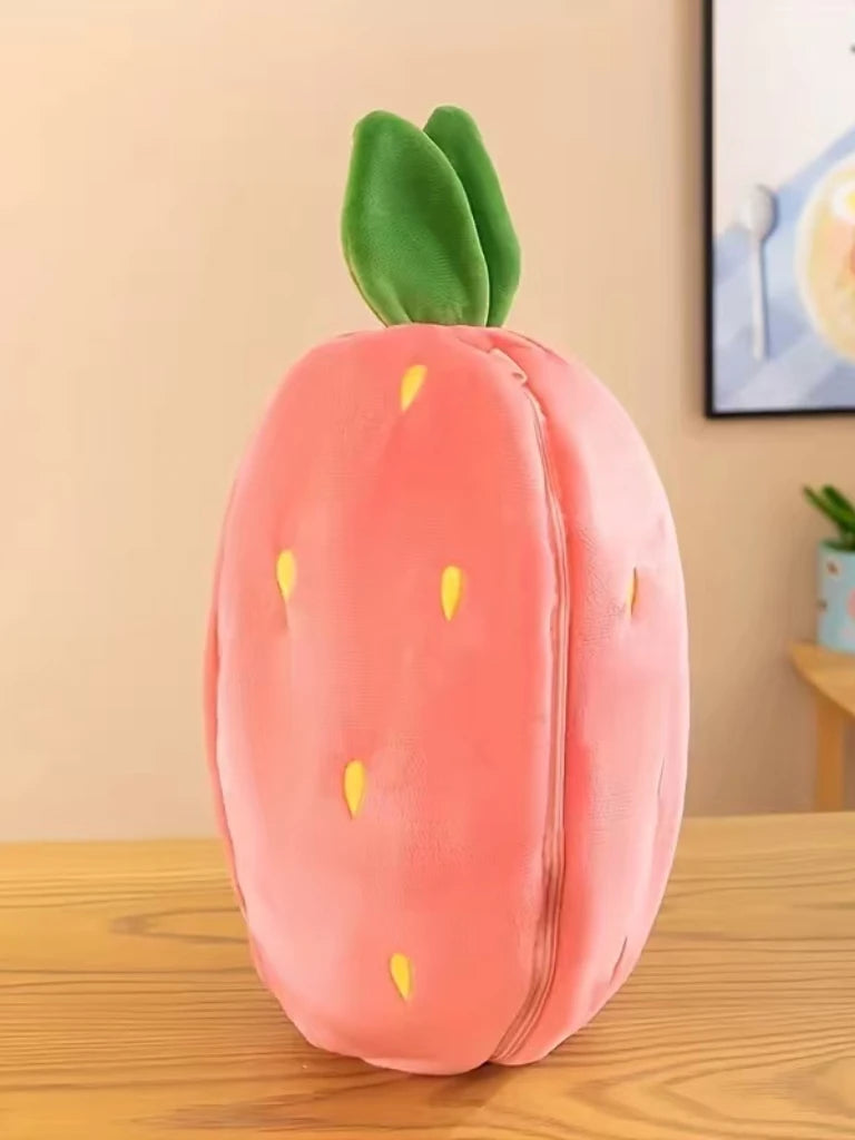 A pink plush strawberry with green leaves and a bunny-shaped pillow on a wooden surface.