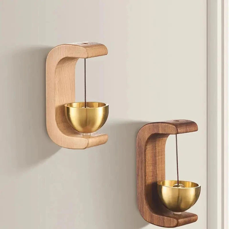 A pair of wooden wind chime doorbells with brass bowls mounted on a wall.