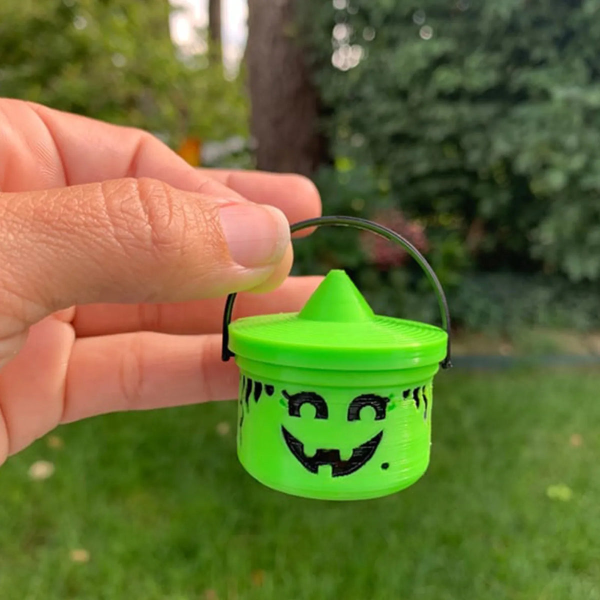 A hand holds a miniature pumpkin Halloween bucket for treats and decor with a carved face in bright lime green.