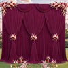 A deep magenta fabric backdrop with draped curtains and floral accents for an event setting.