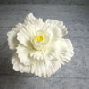A white silk foam rose flower with yellow center is displayed on a gray surface.