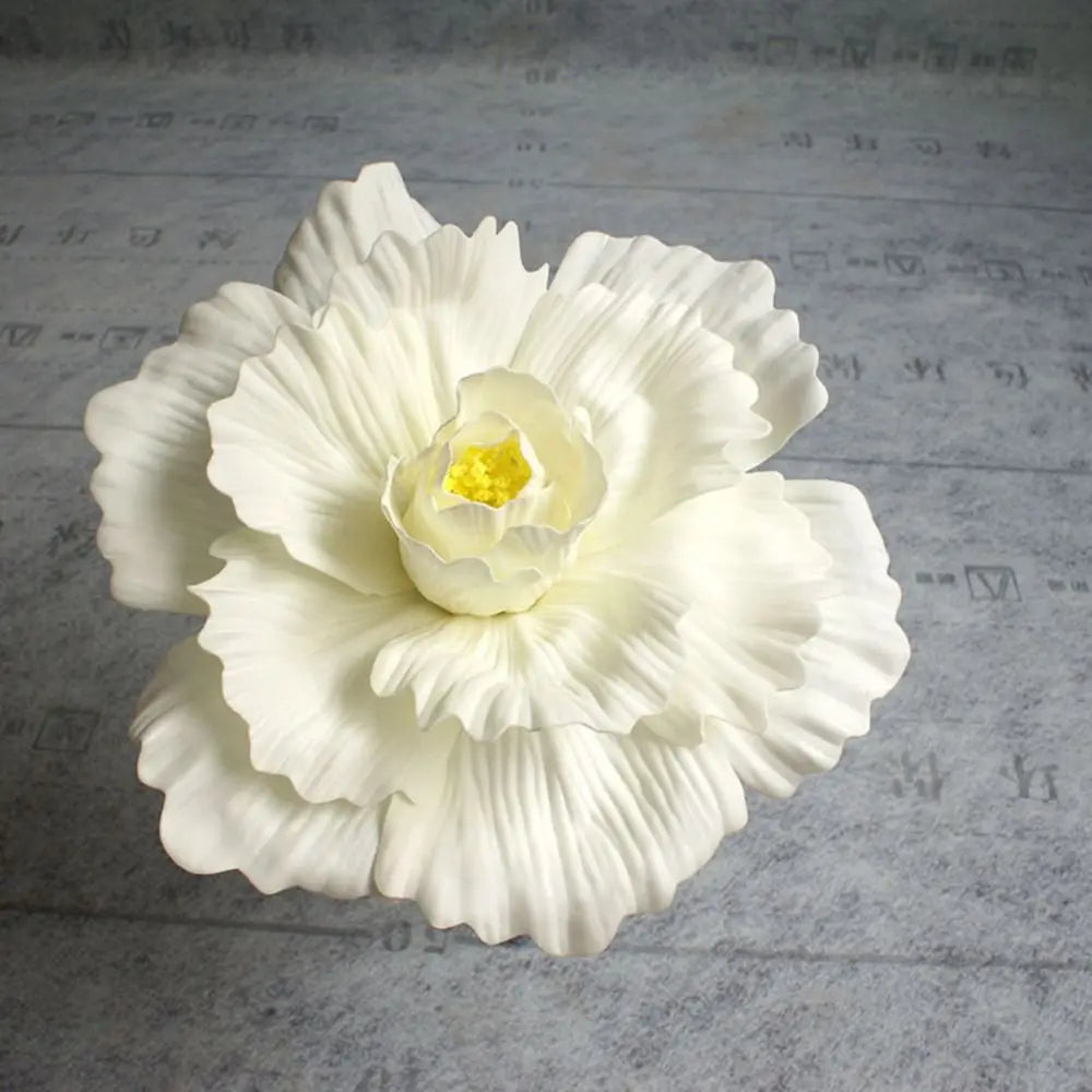 A white silk foam rose flower with yellow center is displayed on a gray surface.