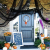 A dark fabric draped over a door decorated with skulls and pumpkins, set against a brick wall.