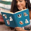 A teal notebook open to show various cat vinyl decals featuring different cats and a brick design.