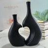 A black ceramic vase with a modern heart shape is displayed on a white marble surface.