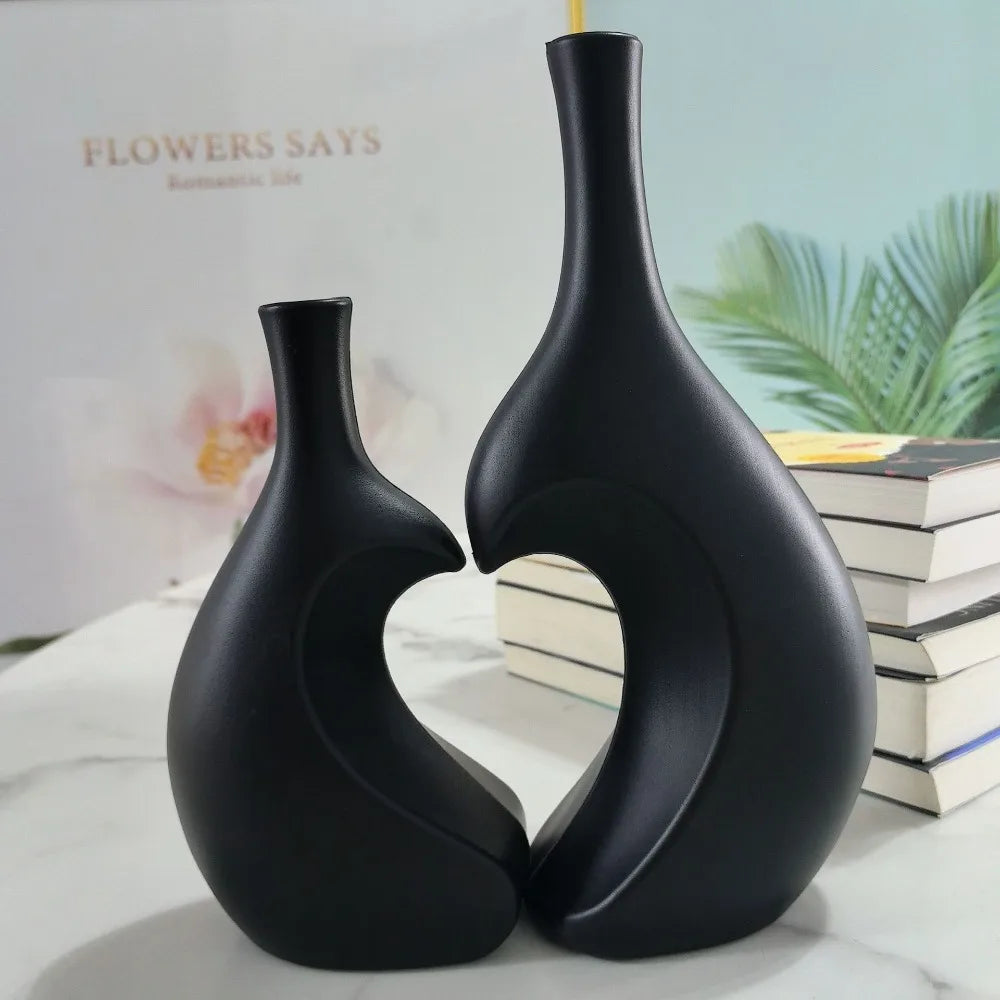 A black ceramic vase with a modern heart shape is displayed on a white marble surface.
