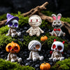 A set of Halloween resin figurines depicting skeletons, mummies, and a rabbit, arranged on moss and black stones.