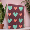 Álbum de recortes de tela morada oscura decorado con corazones repetidos de verde claro y naranja.