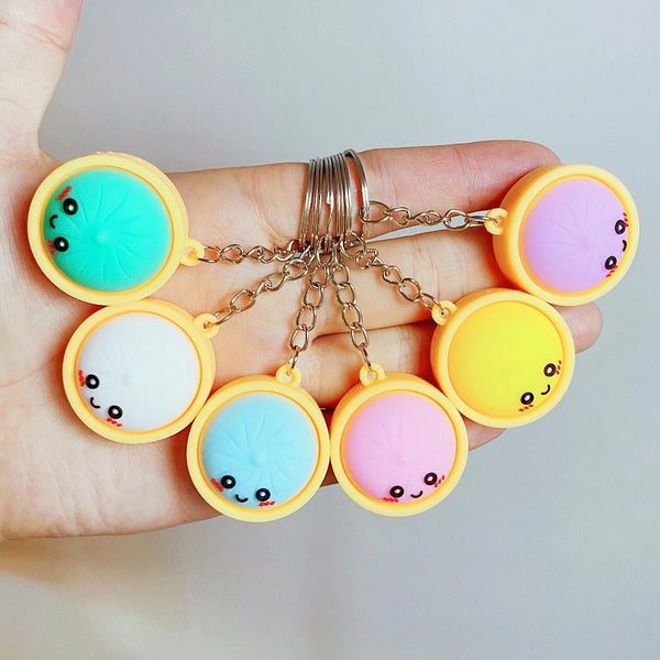 A hand holds several colorful charm keychains featuring cute food faces in yellow, pink, and teal.